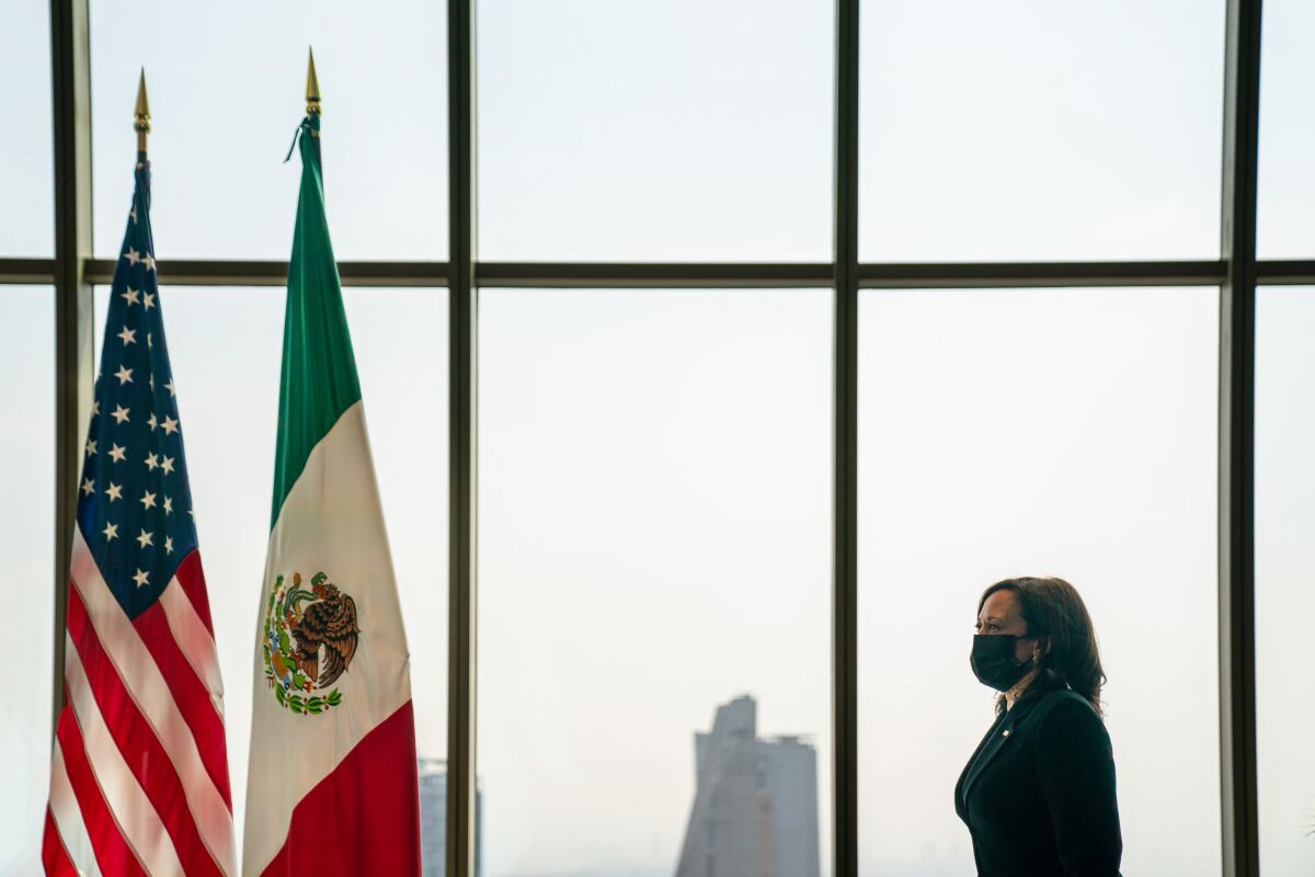 Vice President Kamala Harris walks past a window near two flags.