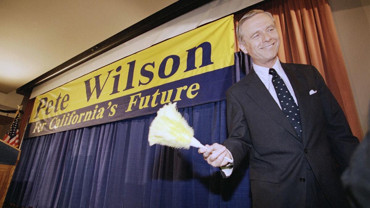 Then-California Gov. Pete Wilson smiles after being handed a feathered duster following a news conference in Los Angeles, Nov. 9, 1994.