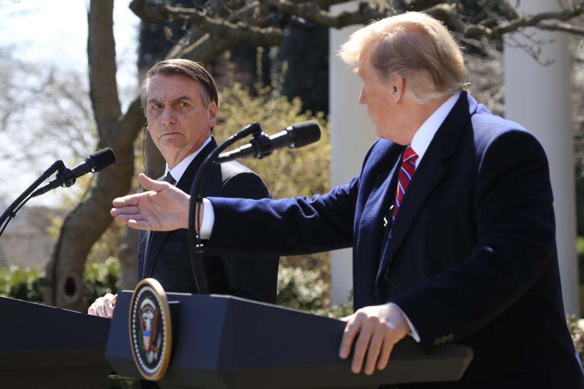 President Trump gestures while speaking at a lectern outdoors next to Brazilian President Jair Bolsonaro