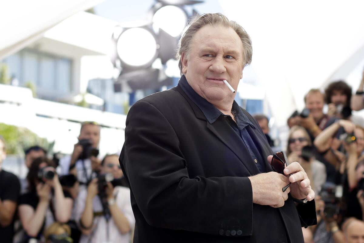 Gerard Depardieu stands in front of a group of photographers with a cigarette dangling from his mouth