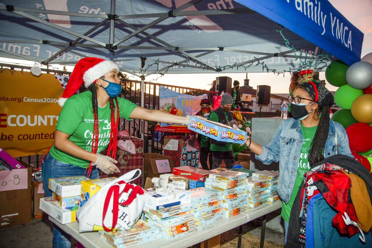 A volunteer wearing a Santa hat hands a box to a woman
