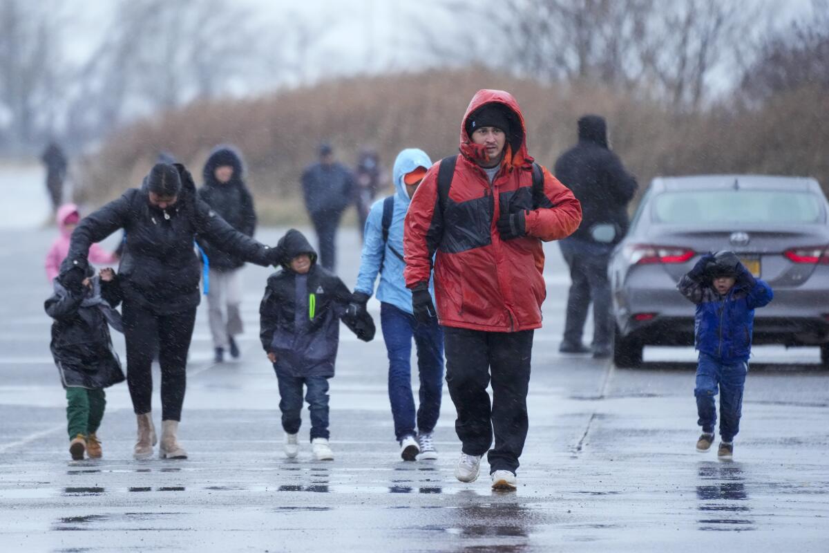 Migrantes corren bajo la lluvia hacia las carpas instaladas en el antiguo aeropuerto Floyd Bennett Field, 