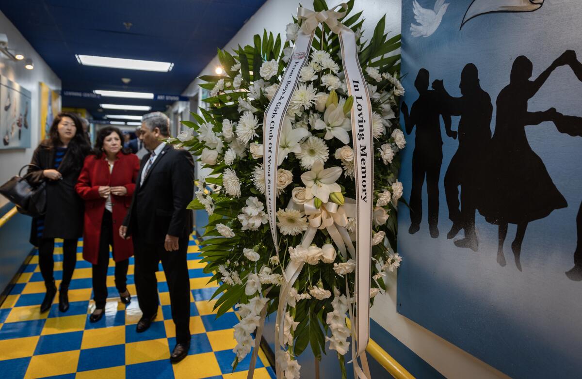 A woman in a red jacket is flanked by another woman and a man near a display of white flowers indoors 