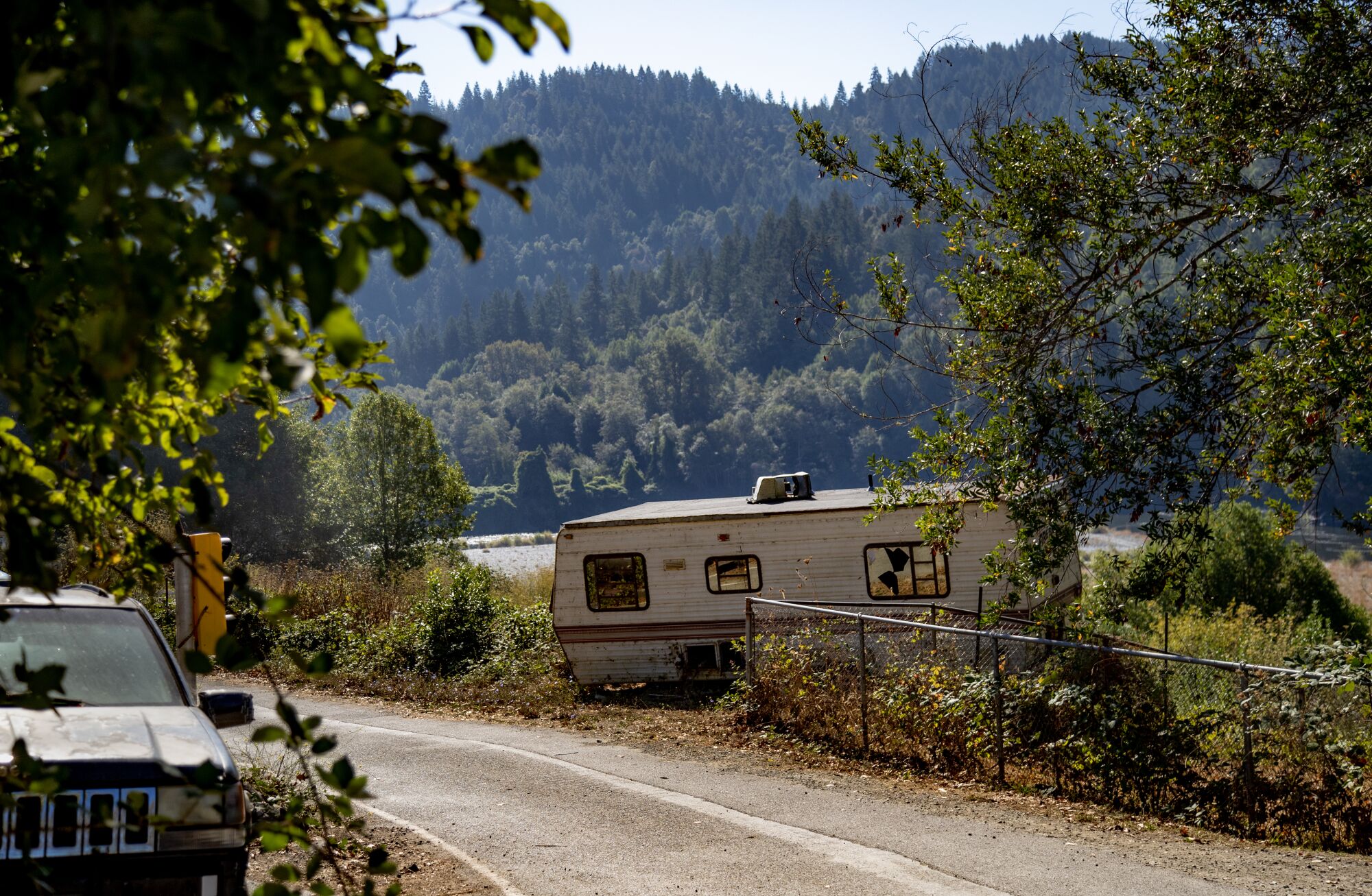 A run-down motor home near a road surrounded by forests.