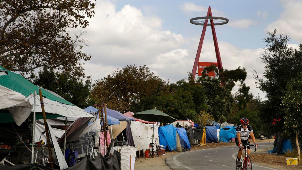 A cyclist passes the row of tents and tarps along the Santa Ana riverbed near Angel Stadium in September.