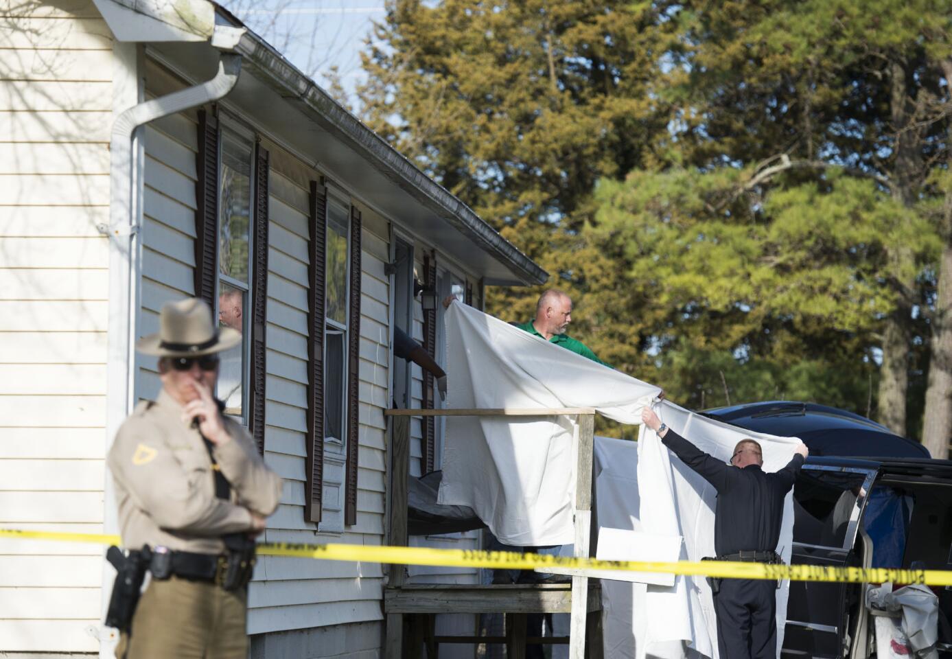 Sheets are held as a body is removed from a residence where police say seven children and one adult have been found dead Monday, April 6, 2015, in Princess Anne, Md.