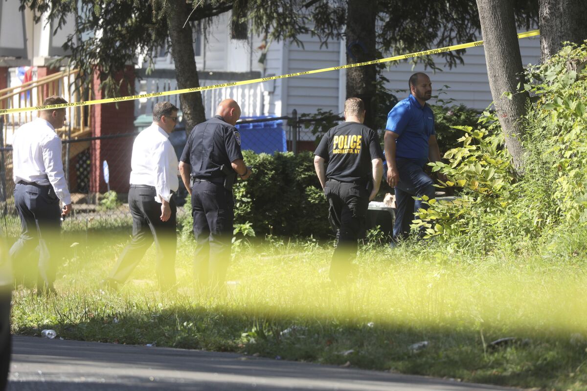 Rochester police investigate behind a house on the corner of Bauman and Laser Streets where two police officers were shot last night in this area in Rochester, N.Y., on Friday, July 22, 2022. (Tina MacIntyre-Yee/Democrat & Chronicle via AP)