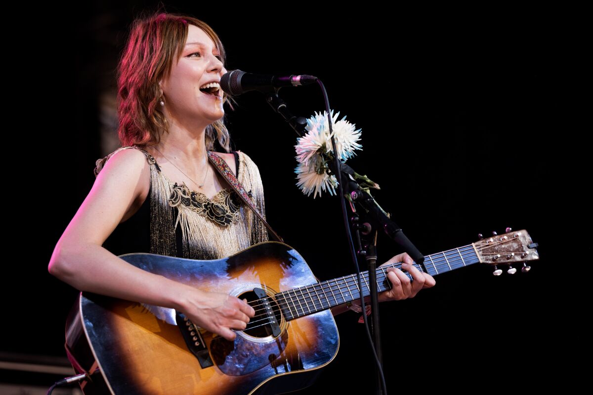 A female musician sings and plays acoustic guitar onstage