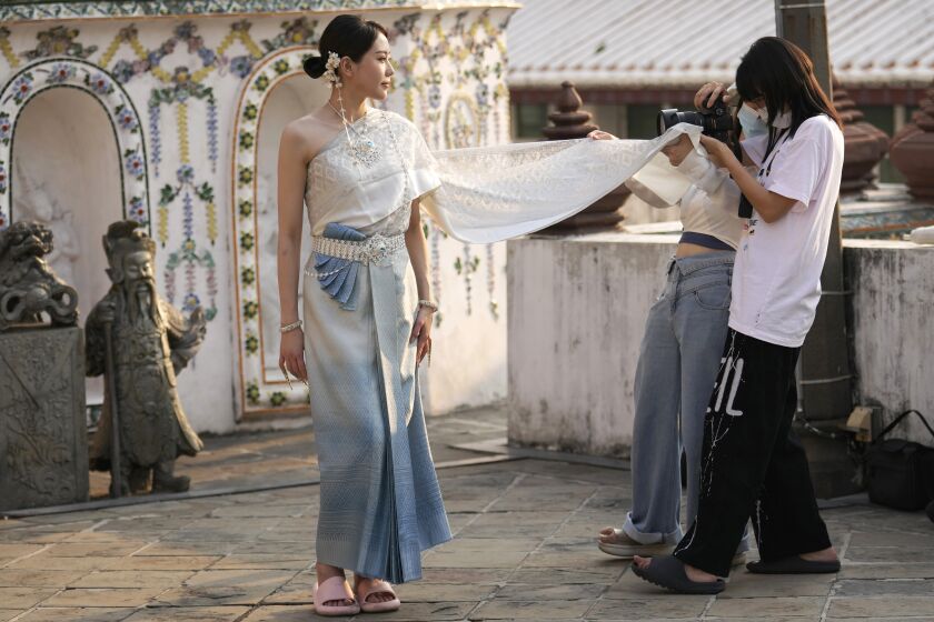 A Chinese tourist in traditional Thai costume poses for a photograph at Wat Arun or the "Temple of Dawn" in Bangkok, Thailand on Jan. 12, 2023. A hoped-for boom in Chinese tourism in Asia over next week’s Lunar New Year holidays looks set to be more of a blip as most travelers opt to stay inside China if they go anywhere. (AP Photo/Sakchai Lalit)