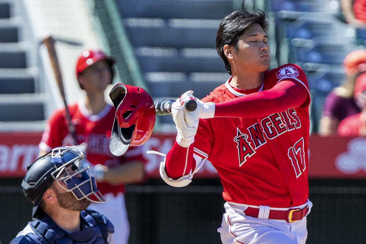 Angels designated hitter Shohei Ohtani, right, knocks off his helmet while fouling off a pitch.