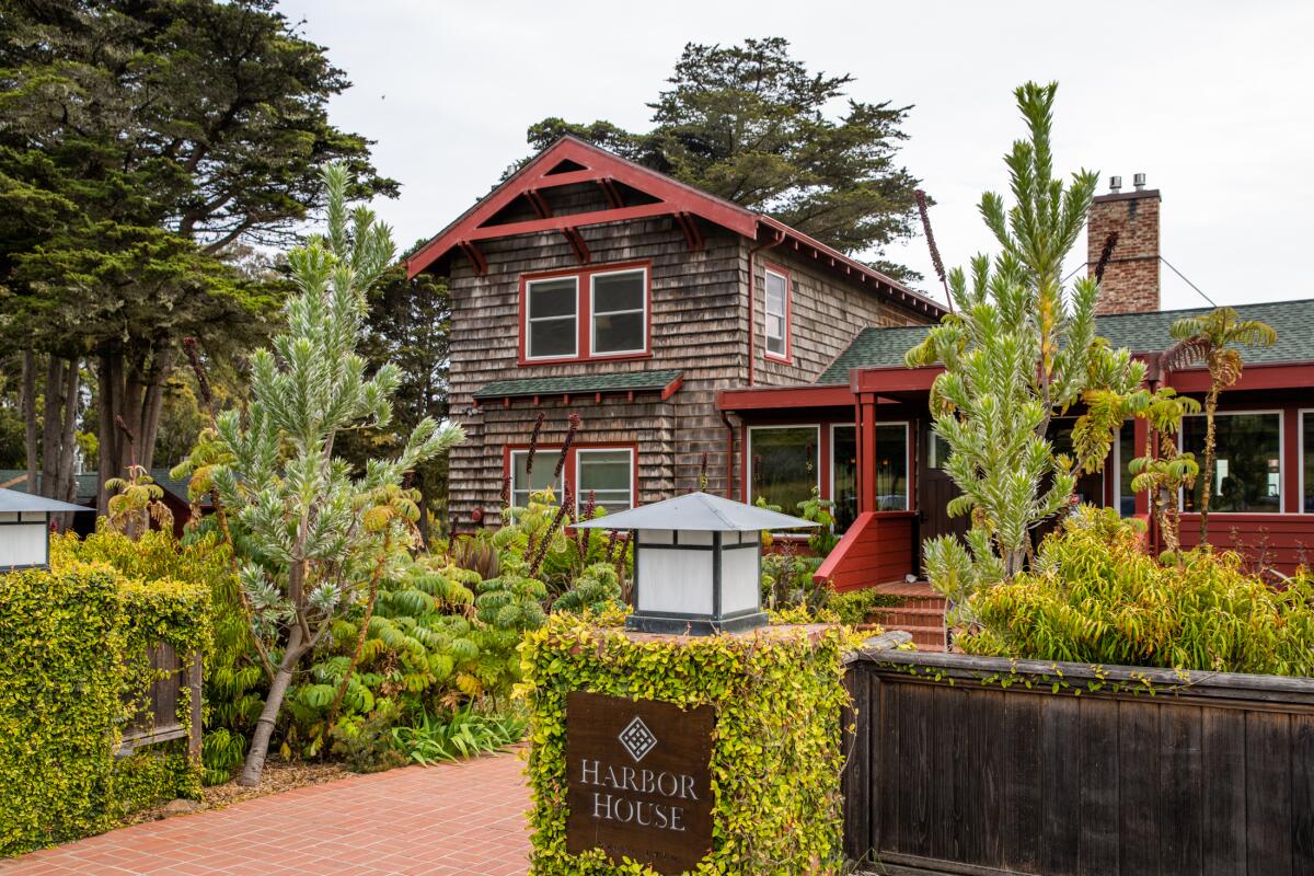 An exterior shot of a two-story building with wood shingles and red trim, surrounded by shrubs and trees.