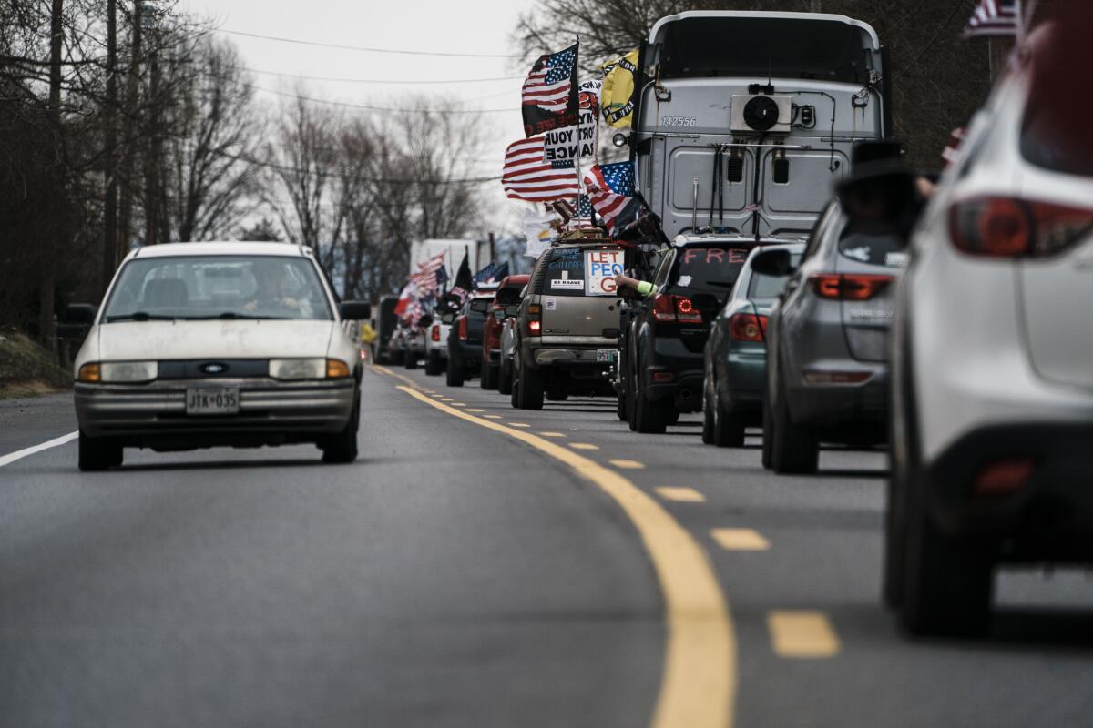 A car drives in one lane as a line of trucks and other vehicles with flags drives in the other