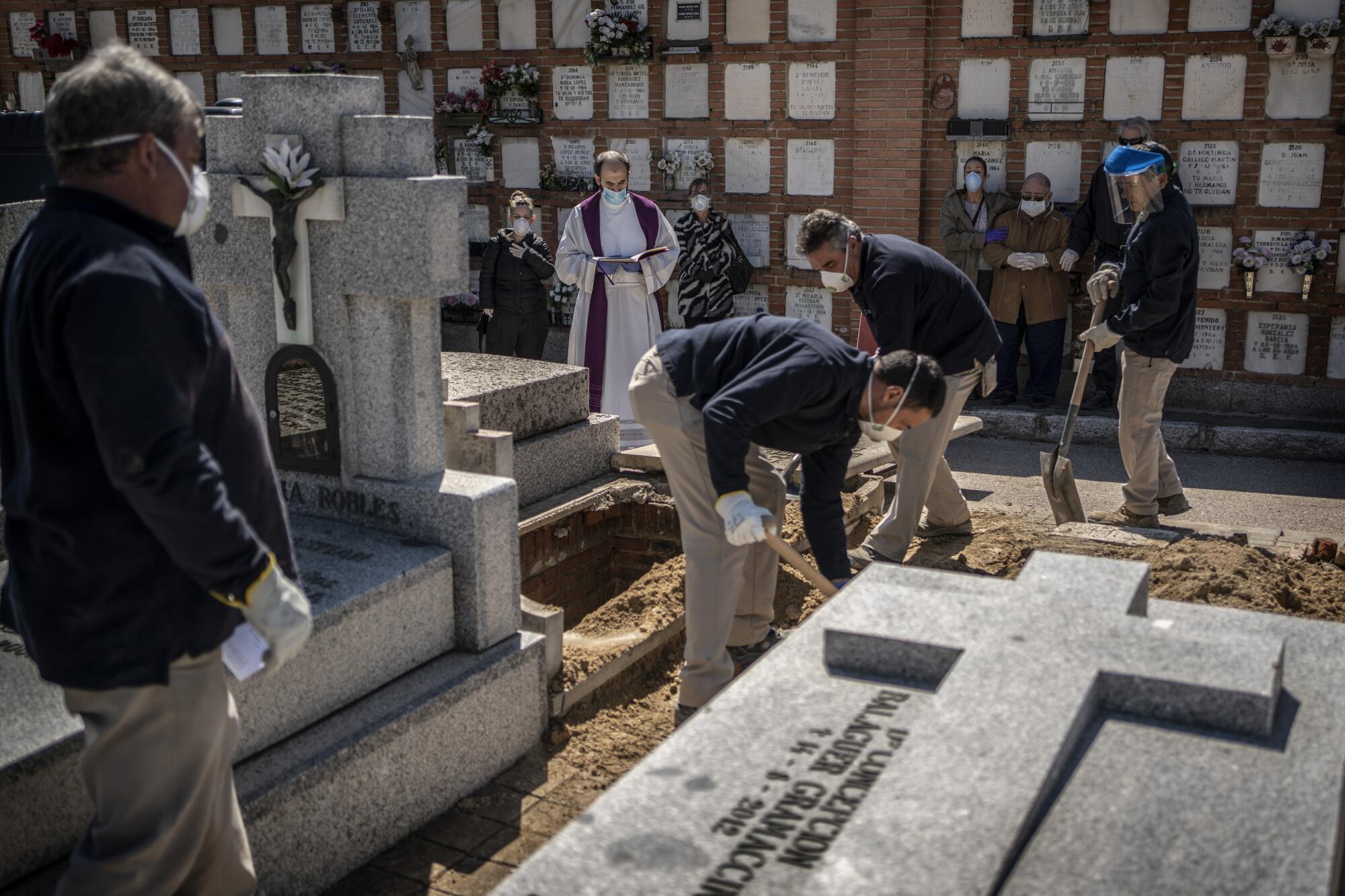 SPAIN:  A priest and relatives pray as a COVID-19 victim's coffin is buried at the Almudena cemetery in Madrid.