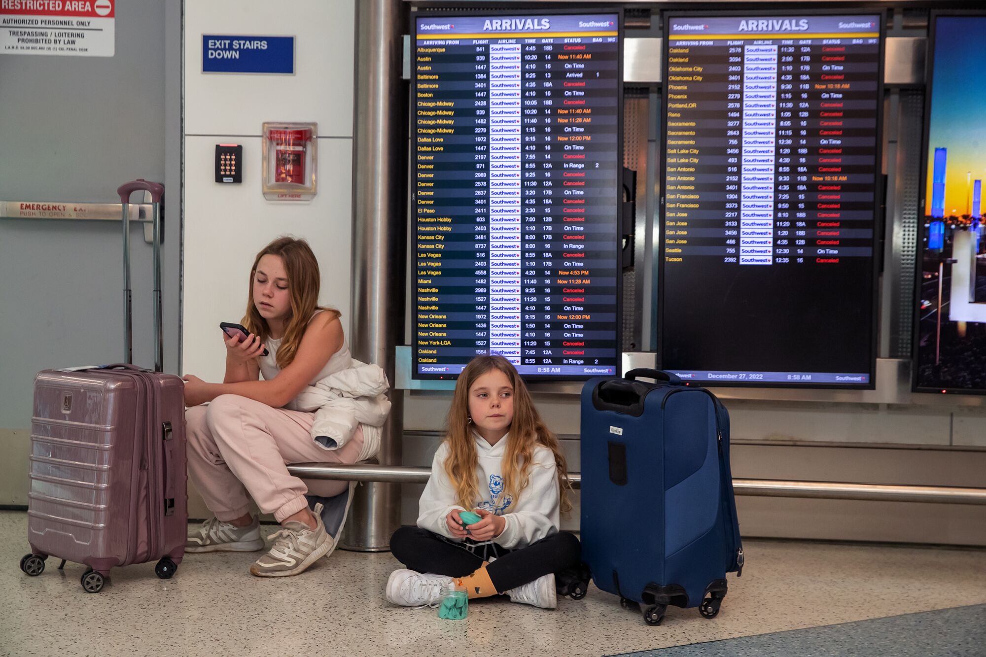 Two girls wait with their bags at an airport.