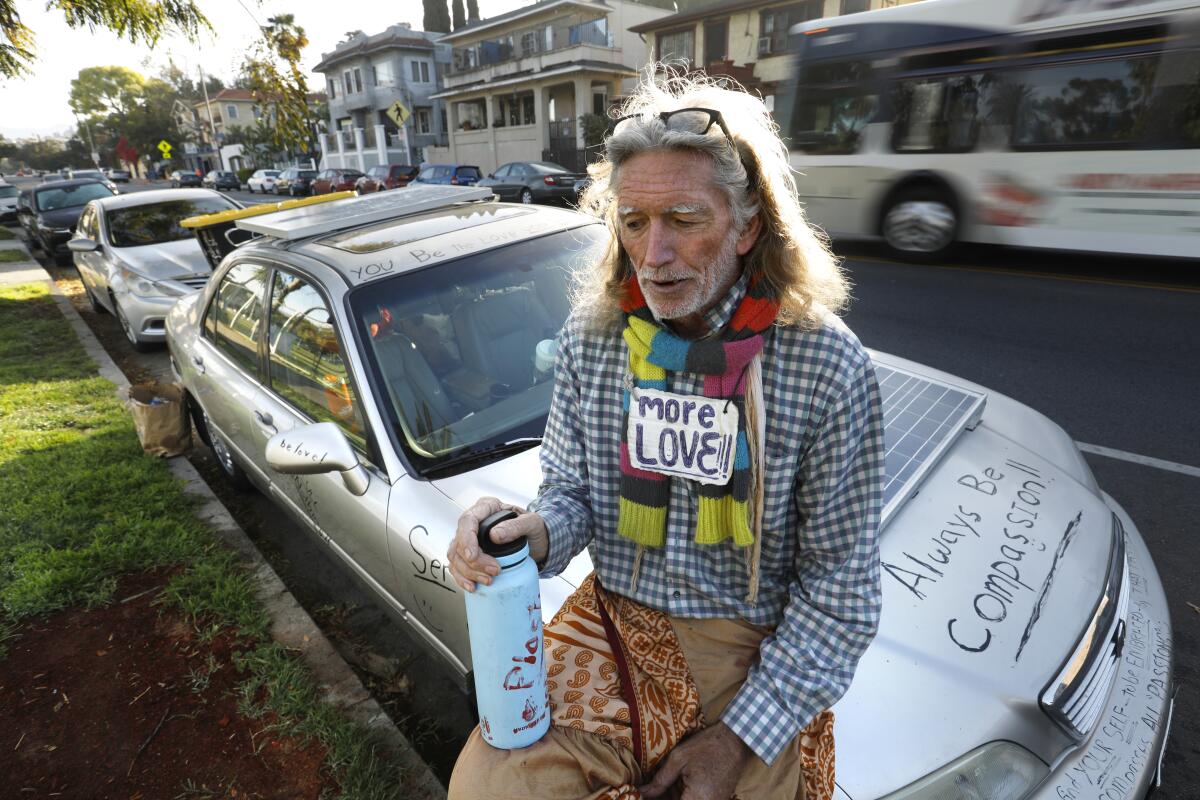 David Busch-Lilly sits on the hood of his vehicle with the message, "Always Be Compassion!!"