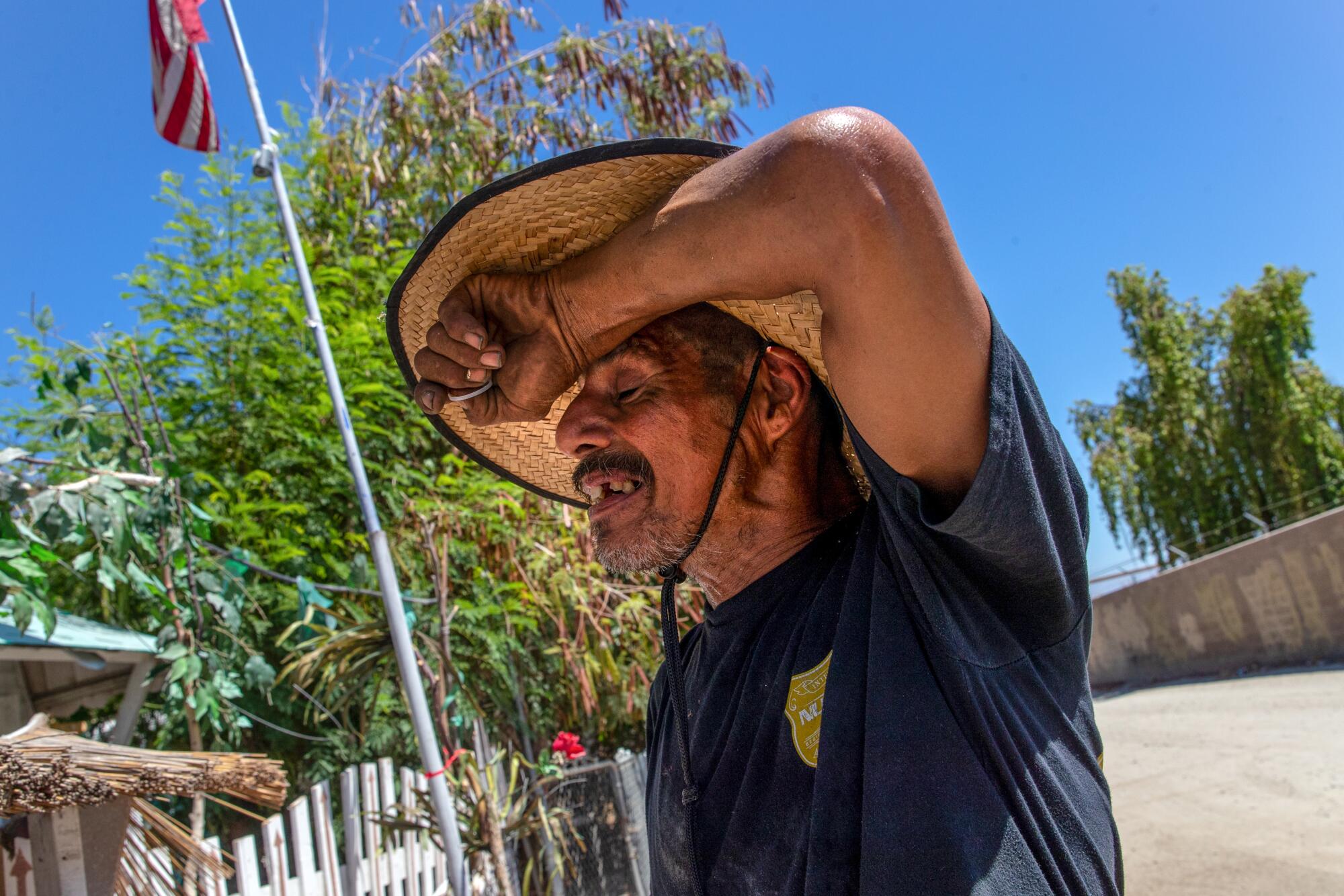 A man in a hat wipes his brow while working under the blazing sun at a mobile home park in Thermal, Calif.