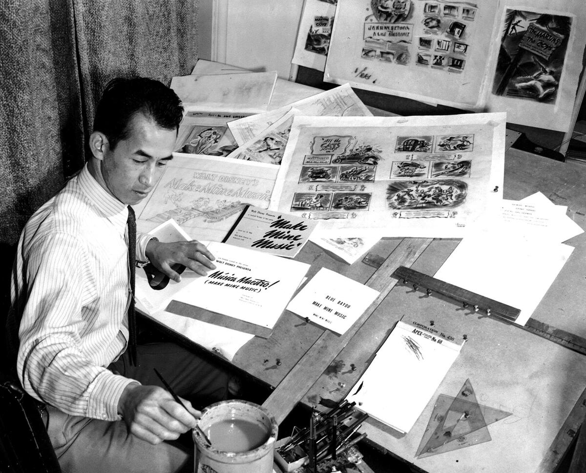 
A black-and-white portrait of an animator dabbing a brush at a desk filled with papers