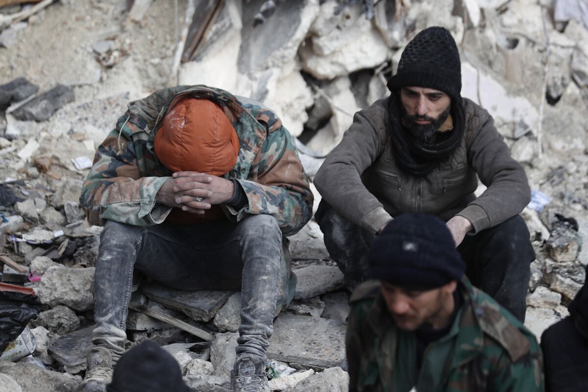 People react as they sit on the wreckage of collapsed buildings, in Aleppo, Syria, Tuesday, Feb. 7, 2023. Rescuers raced Tuesday to find survivors in the rubble of thousands of buildings brought down by powerful earthquake and multiple aftershocks that struck eastern Turkey and neighboring Syria. (AP Photo/Omar Sanadiki)