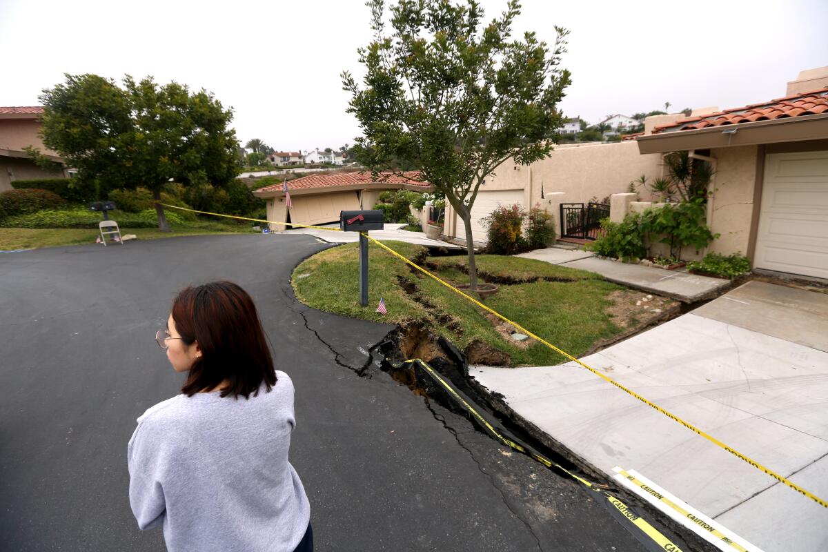 Sooyun Cho stands next to her damaged home, right, on Peartree Lane in Rolling Hills Estates on Sunday.