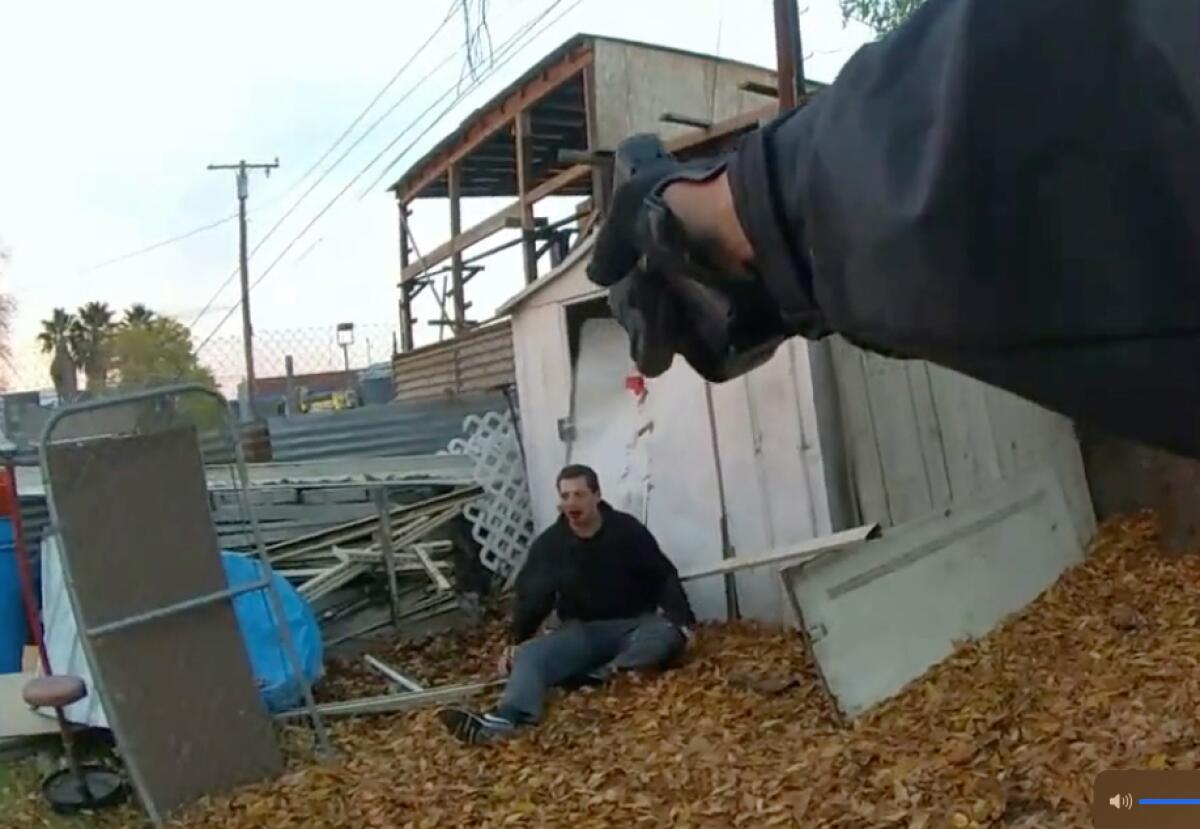 A still from body-camera footage shows an officer aiming at Robert Brown, who is seated on leaves and bleeding from the mouth