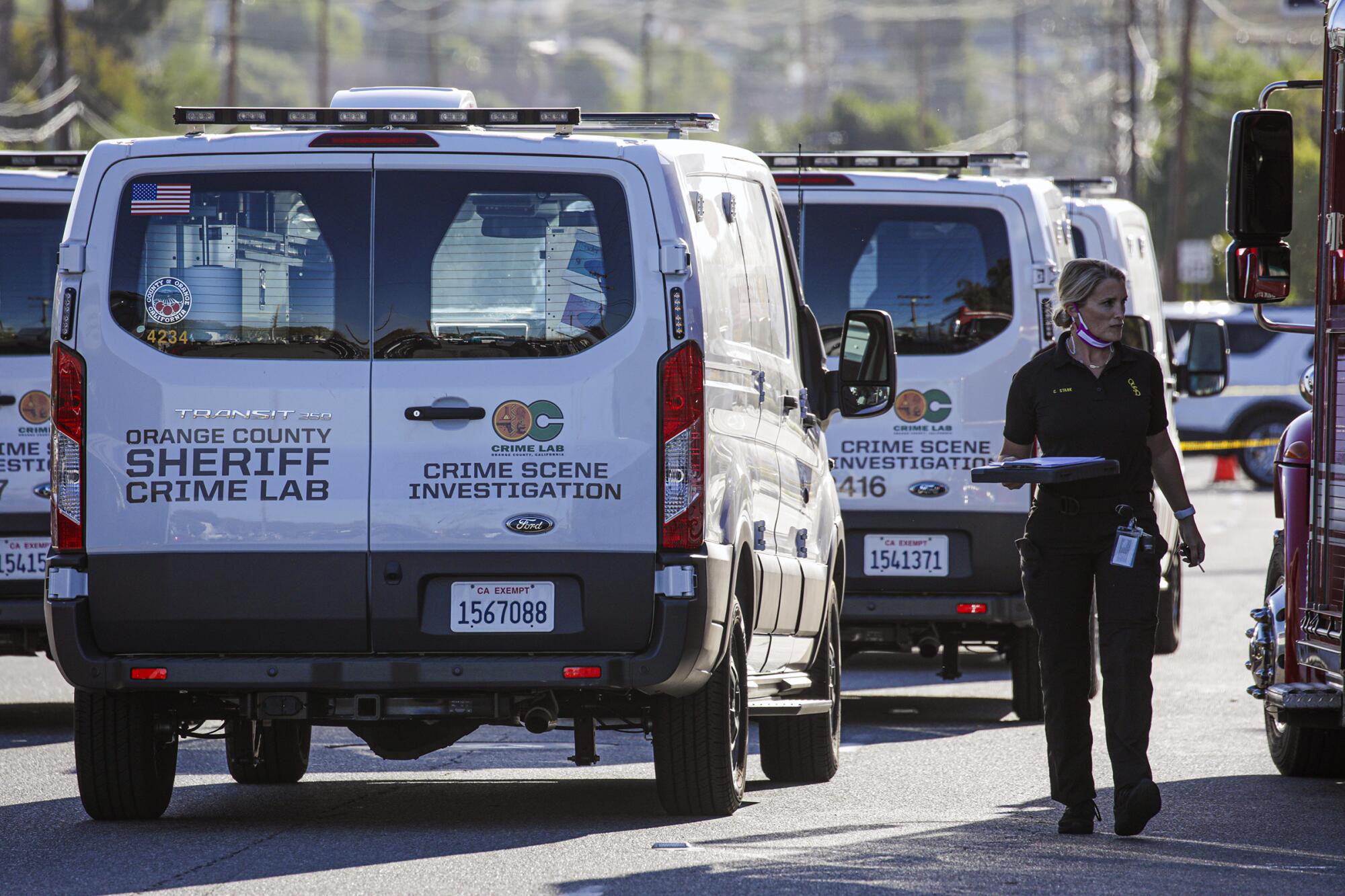 A woman with a clipboard walks alongside a van marked "Orange County sheriff crime lab: Crime scene investigation."