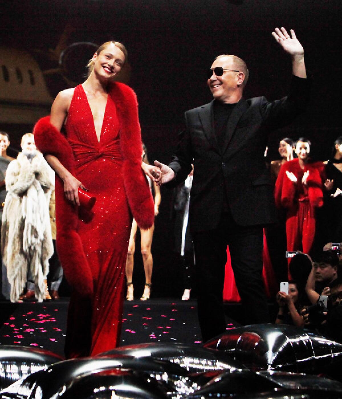 Michael Kors with Karmen Pedaru waves to guest after the fashion show for a picture after The Michael Kors Jet Set Experience fashion show.