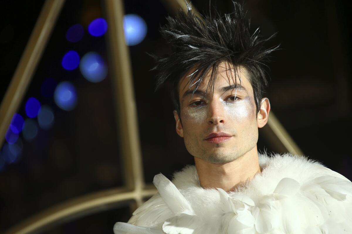 A person with spiked black hair wearing bright highlighter on their cheeks and a white feathered top