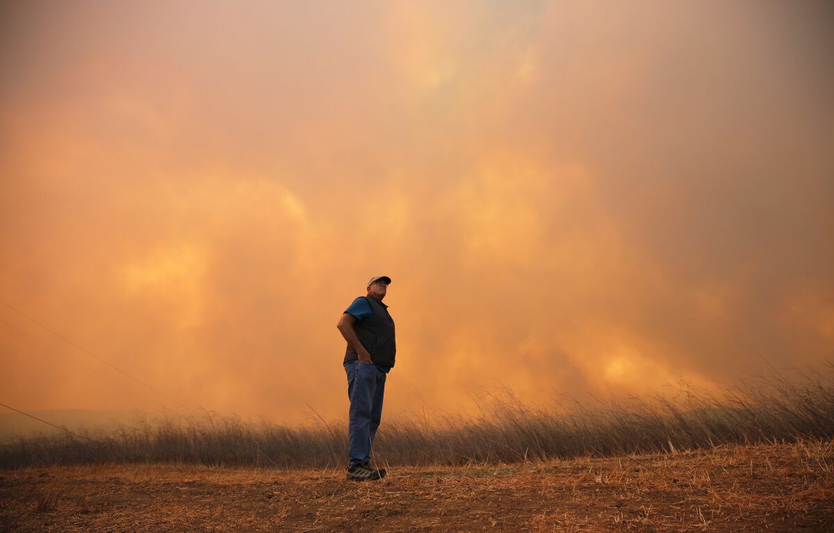 A man stands watching orange flames and smoke