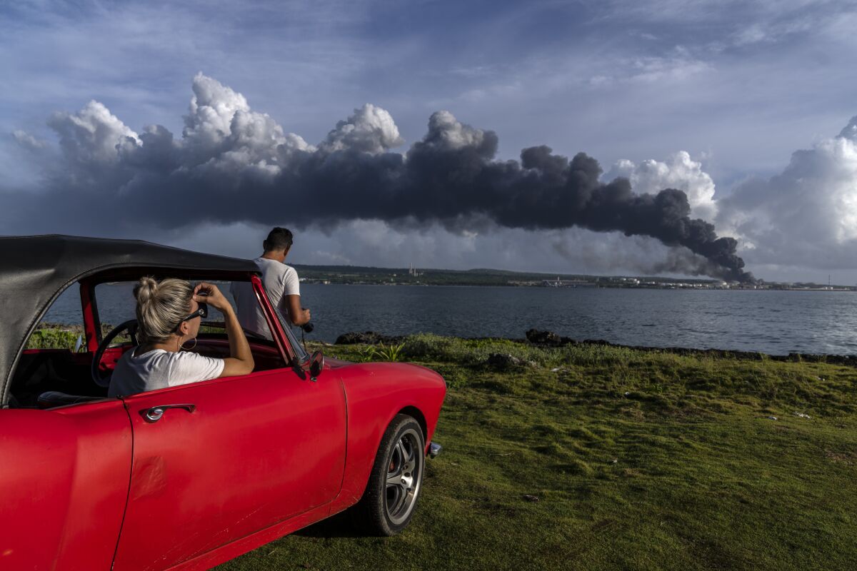 People watch a huge plume of smoke rise from the Matanzas supertanker base, as firefighters work to douse a fire that started during a thunderstorm the night before, in Matanzas, Cuba, Sunday, Aug. 7, 2022. Cuban authorities say lightning struck a crude oil storage tank at the base, sparking a fire that sparked four explosions that injured more than 121 people, one person dead and 17 missing. (AP Photo/Ramon Espinosa)