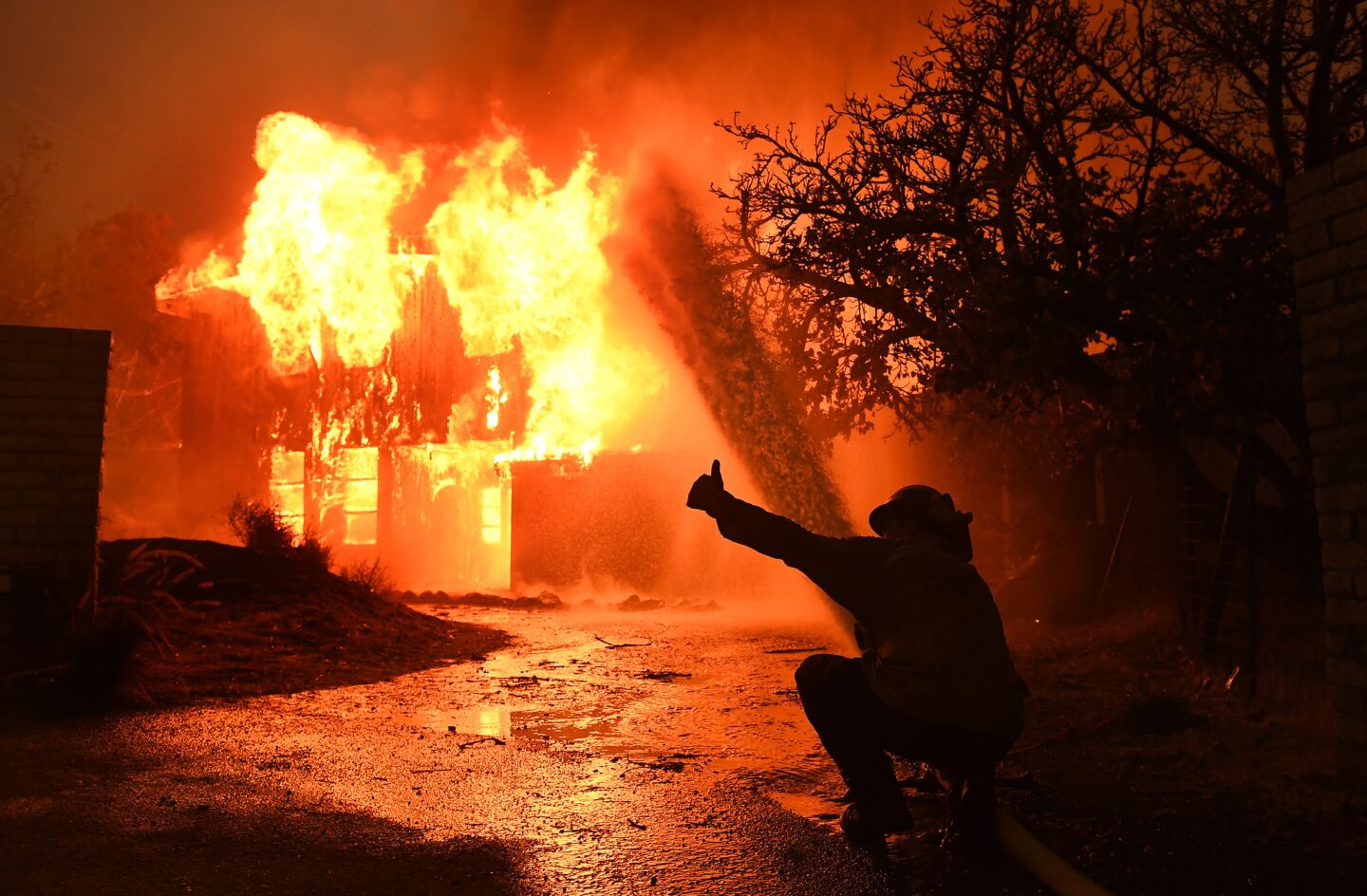 A firefighter requests more water pressure as a house burns from the Woolsey Fire along P.C.H. in Malibu.
