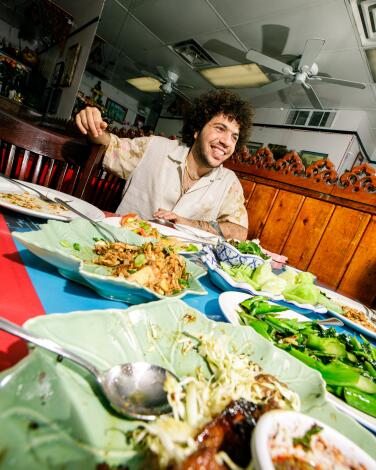 Benny Blanco surrounded by plates of food at Spicy BBQ Restaurant.