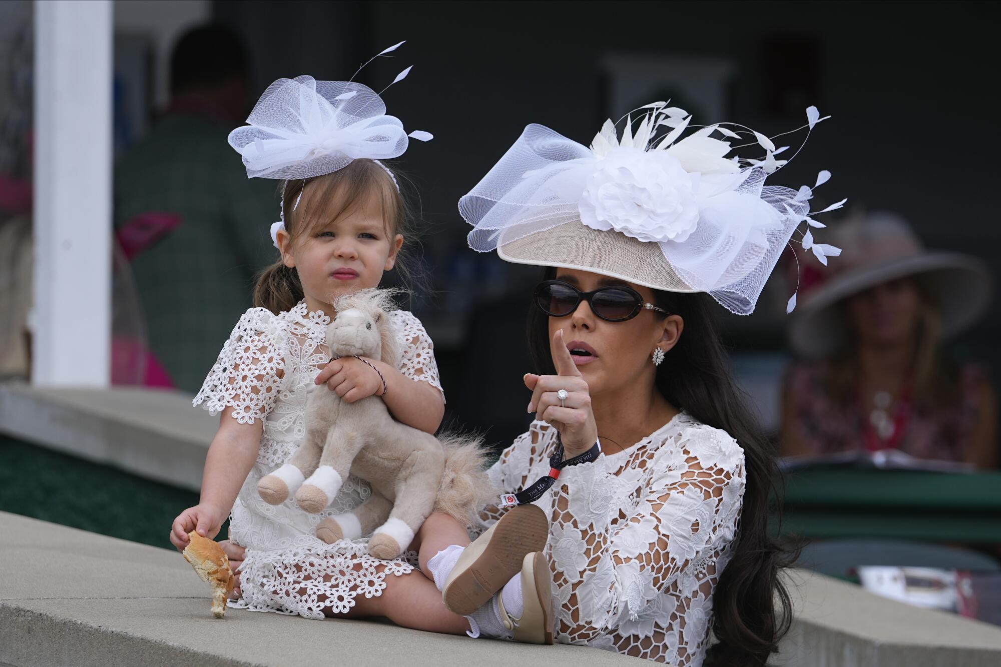 A woman and child wearing hats with distinct decorations wait at Churchill Downs.