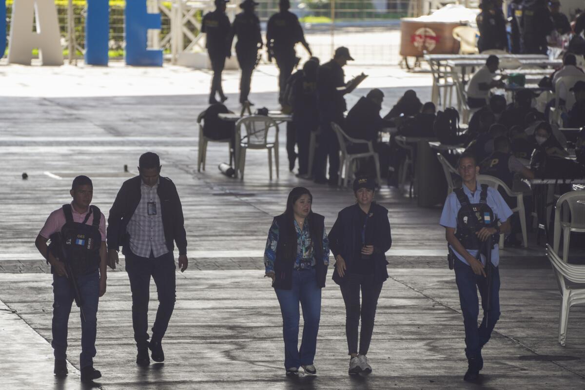 Five people walking side by side past a hub of activity outdoors