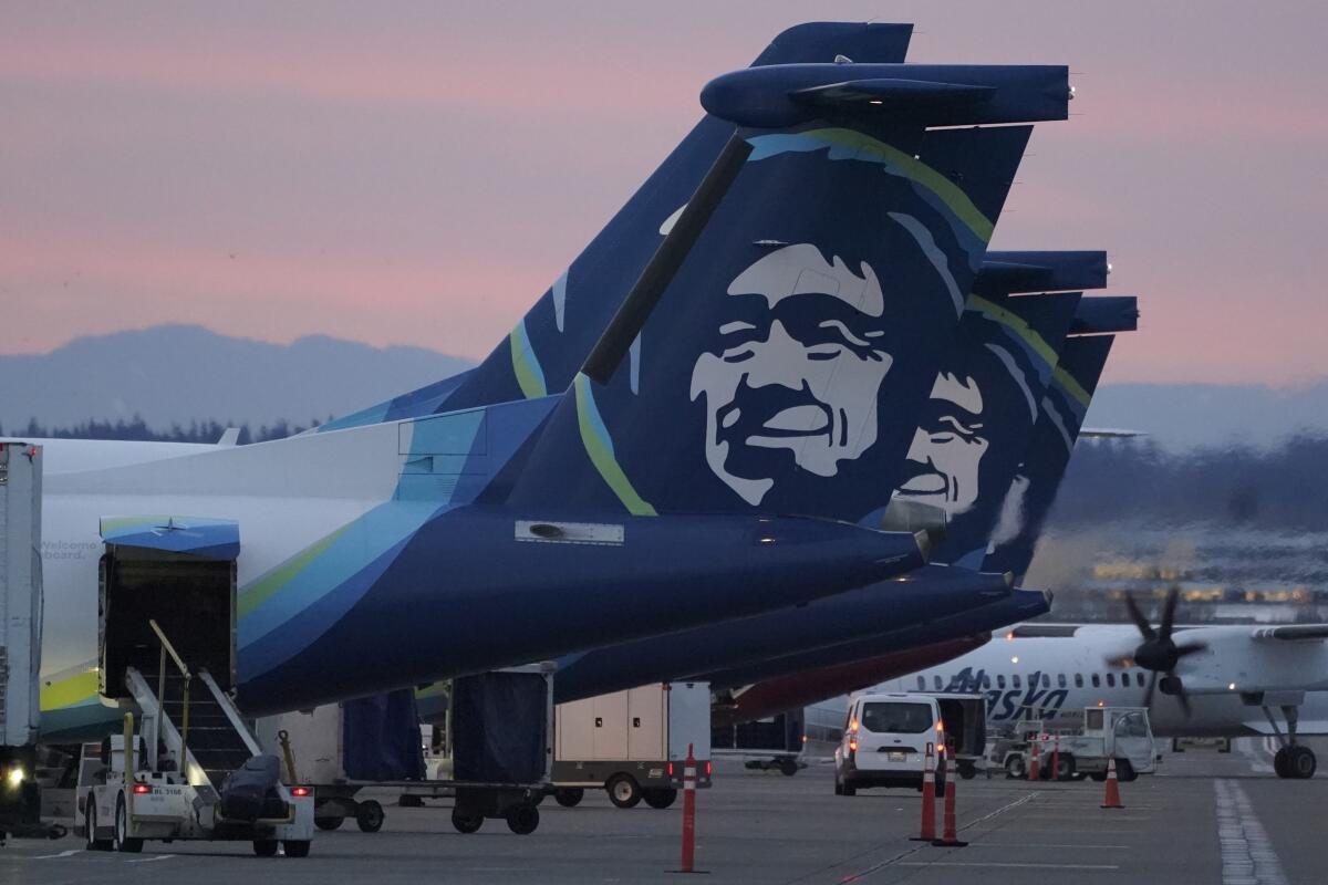The tails of several Alaska Airlines airplanes on a tarmac.