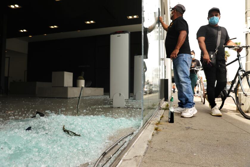 LOS ANGELES-CA-MAY 31, 2020: Shattered glass sits in a storefront on Melrose Avenue as passers by access the damage on Sunday, May 31, 2020. (Christina House / Los Angeles Times)