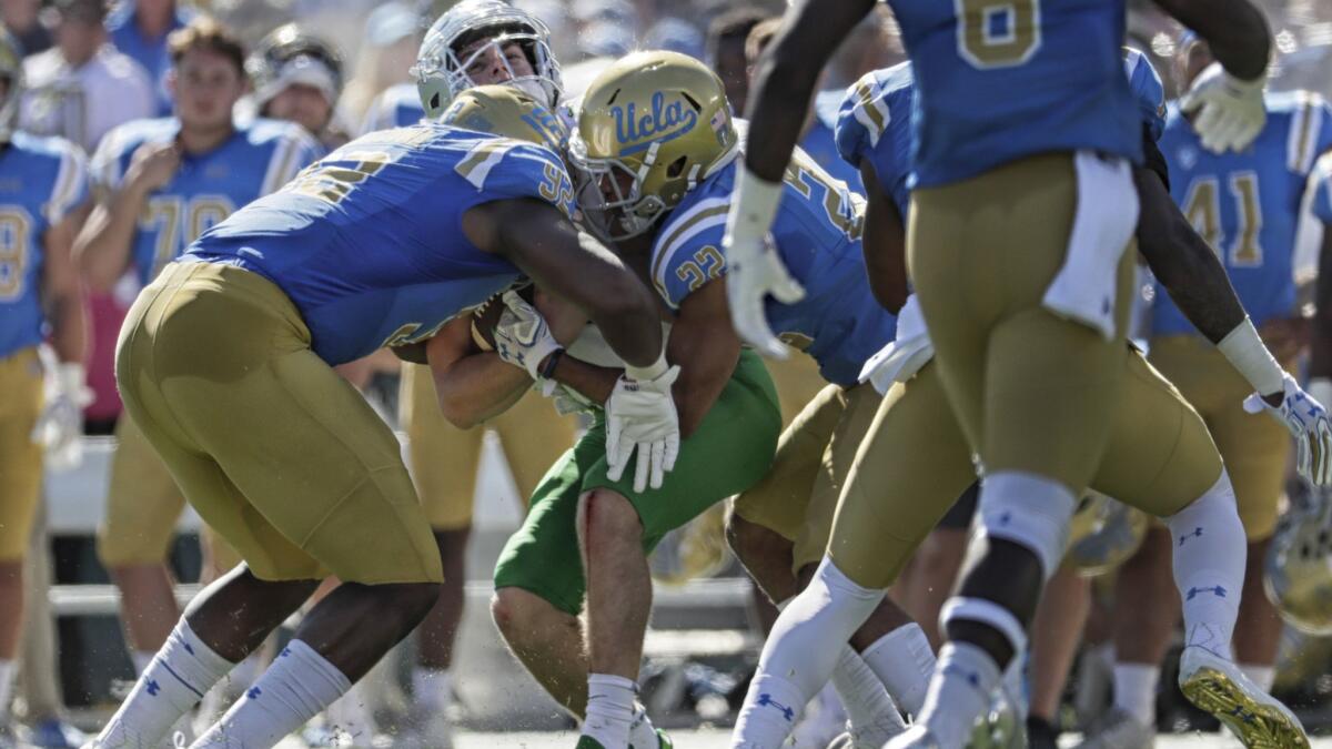 Oregon quarterback Braxton Burmeister is sandwiched by UCLA defenders Osa Odighizuwa, left, and Nate Meadows during a 2017 game at the Rose Bowl.