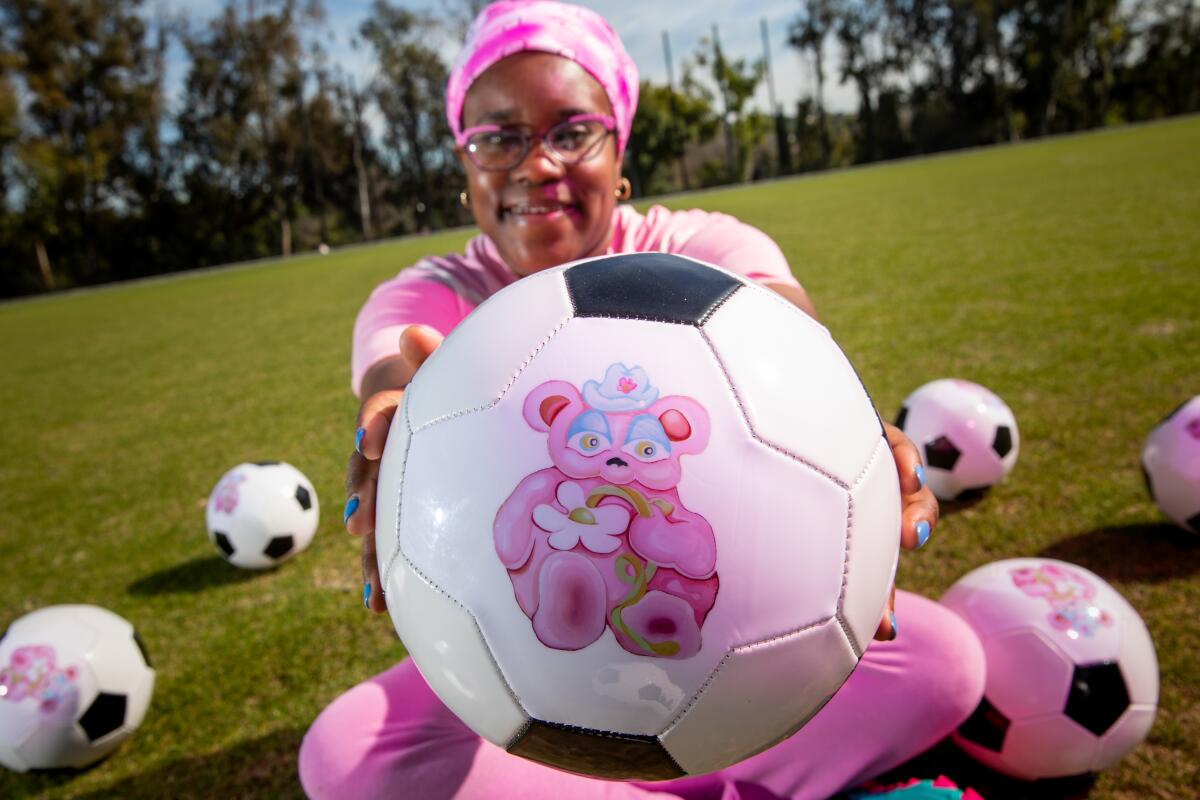 A woman dressed in pink holds a soccer ball with a pink bear on it.