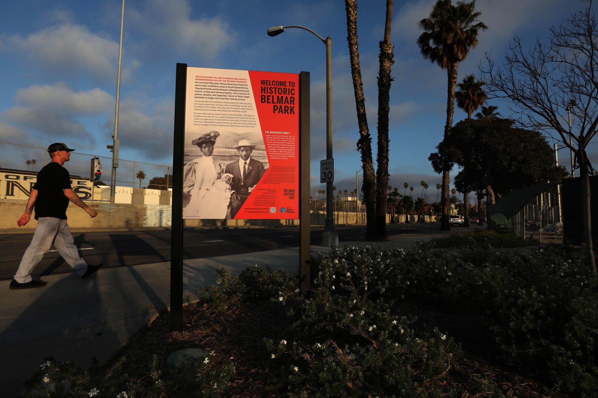 A pedestrian walks past an informational sign along the Historic Belmar Park project in Santa Monica.