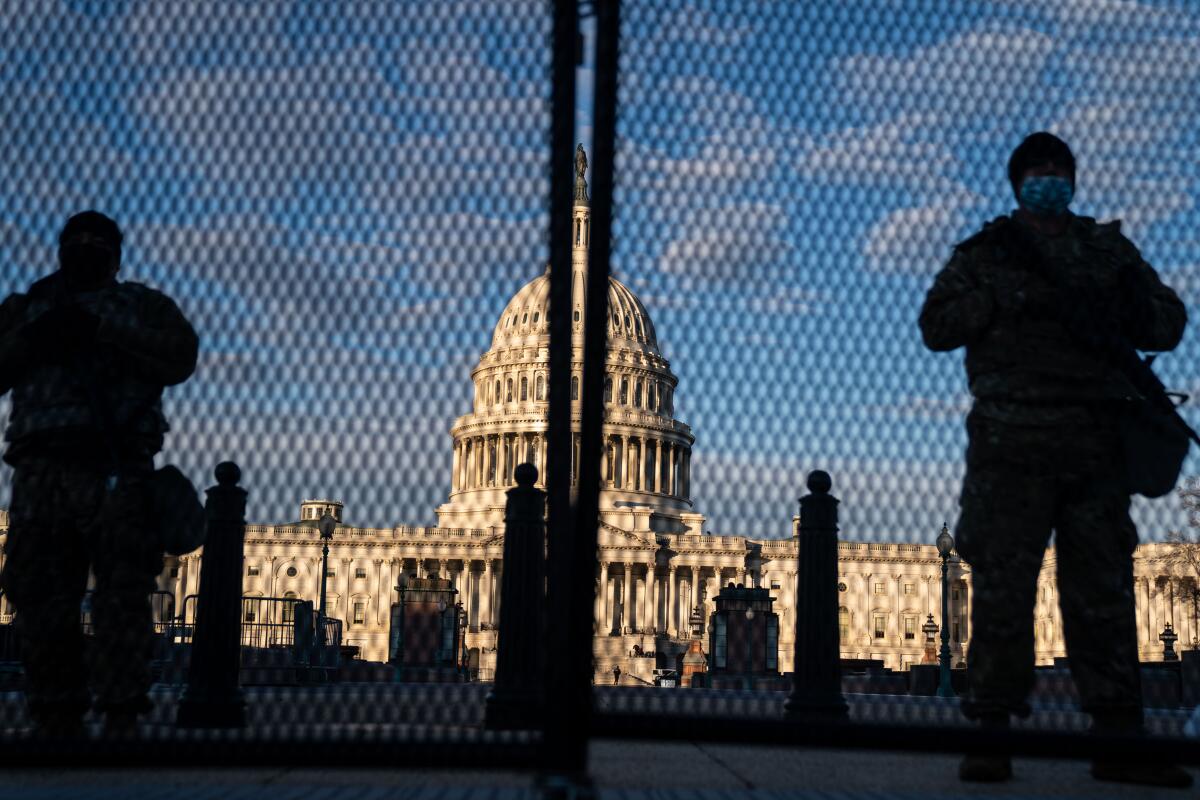 National Guard troops silhouetted behind security fencing with the dome of the U.S. Capitol behind them