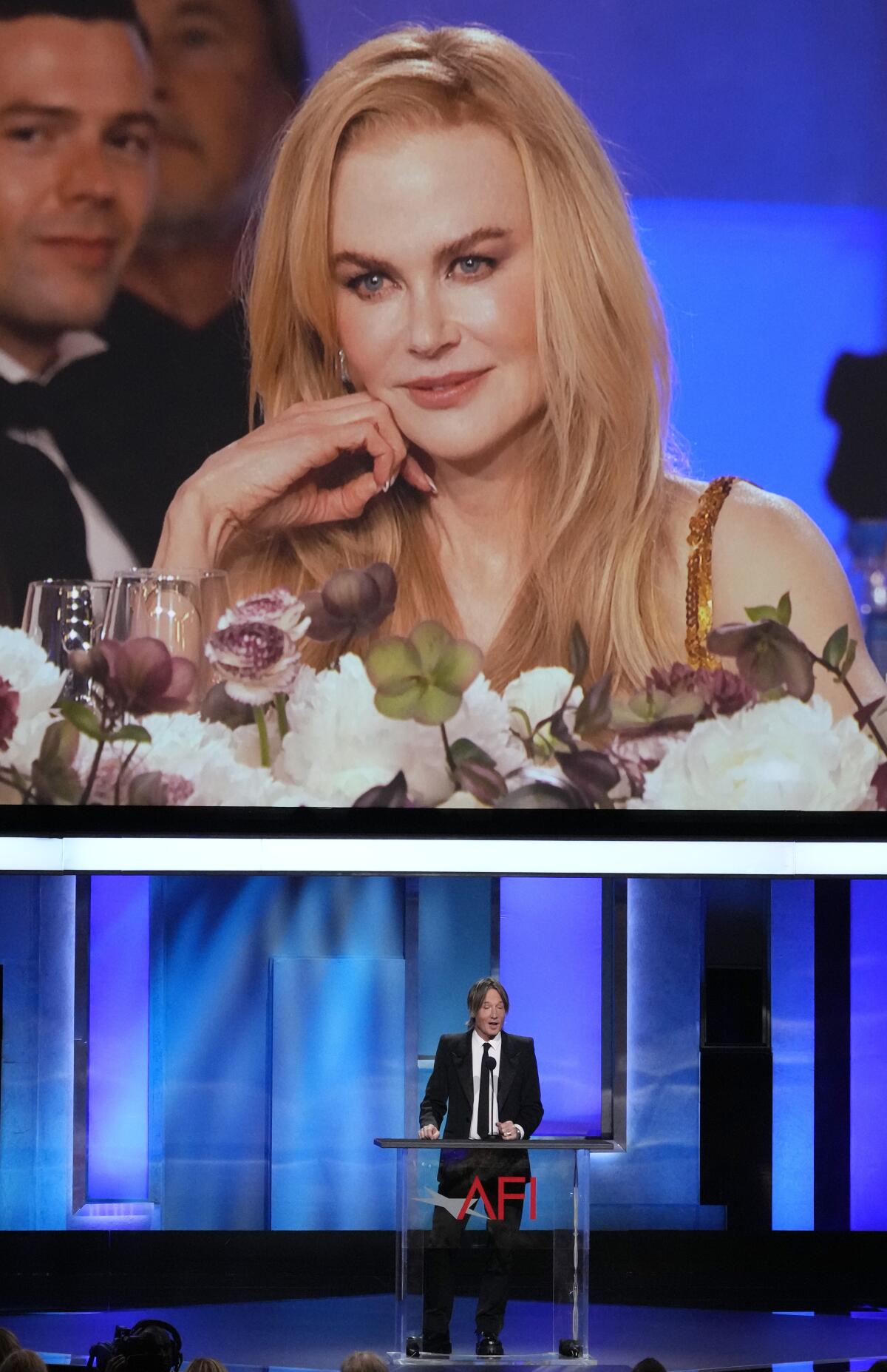 La homenajeada Nicole Kidman aparece en un monitor de video mientras su esposo Keith Urban 