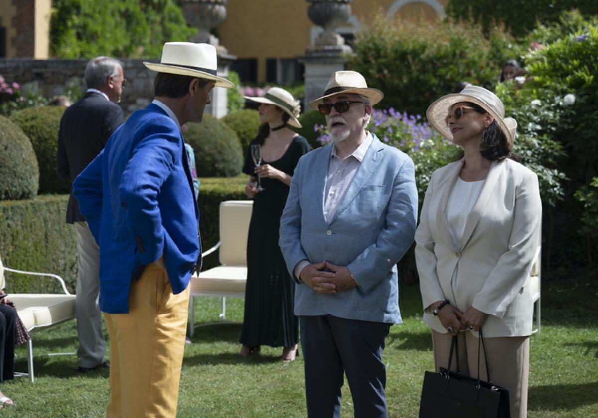 Three people talk in a Tuscan villa's garden in the summer.