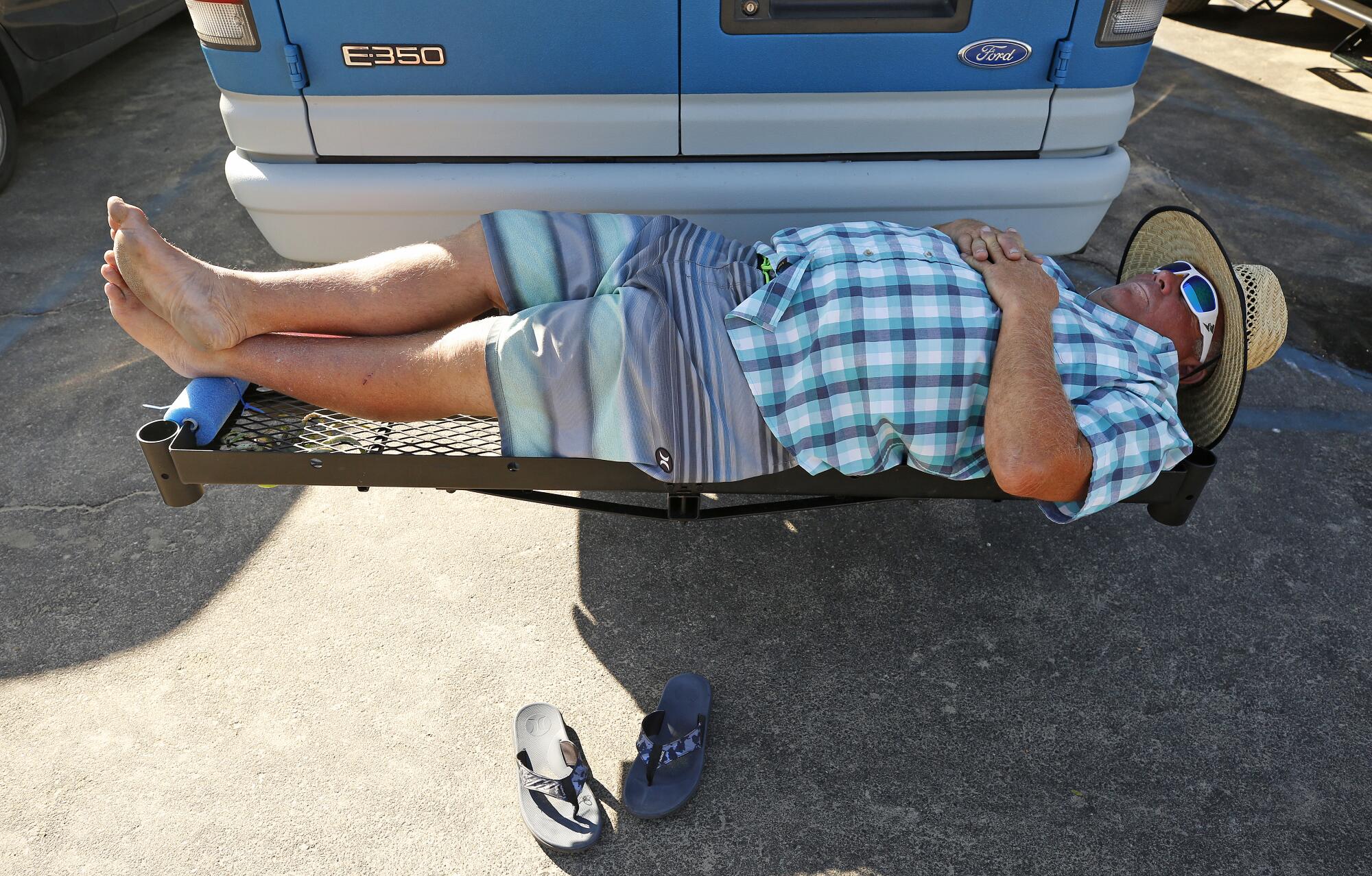 Danny Carr finds some shade and catches a nap on the cargo rack of his van in the warm morning air at Surfrider Beach.