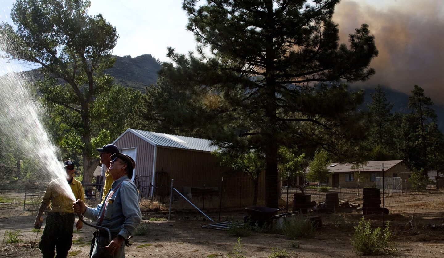 Art Jaenke of Garner Valley hoses down a large shed on his property to prepare as the Mountain fire looms in the background. Jaenke is staying behind to protect his property, despite calls to evacuate.