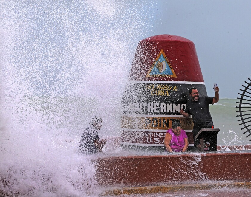 FILE- Key West resident Pedro Lara takes a selfie in front of the Southernmost Point as waves from Hurricane Irma crash over the wall on Sept. 9, 2017. The 20-ton concrete buoy, which marks the Southernmost Point and 90 miles to Cuba, is one of Key West’s famous landmarks. Tourists flock to the marker every day to take photos, snap selfies, buy a souvenir or two.(Miami Herald, Charles Trainor Jr. via AP, File)