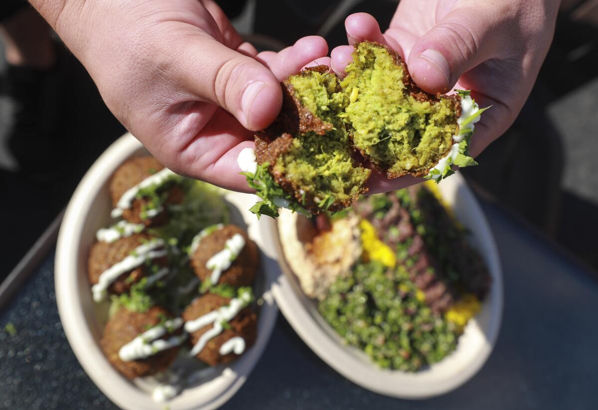 Bryan Zeto, owner and chef of the Shawarma Guys food truck, breaks open a falafel with a Wagyu beef kabob plate and another plate of falafels under.