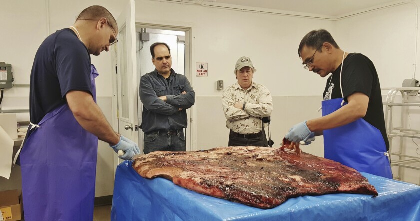 In this Oct. 28, 2016, photo provided by the Maniilaq Association, Alex Whiting, left, and Cyrus Harris, right, are observed by Chris Sannito, second from left, and Brian Himelbloom, third from left, of the Kodiak Seafood and Marine Science Center as they trim and clean seal blubber in Kotzebue, Alaska. In January 2021, the Alaska Department of Environmental Conservation approved seal oil to be served at a Maniilaq elder care home, believed to be a first for seal oil in the U.S. (Maniilaq Association via AP)