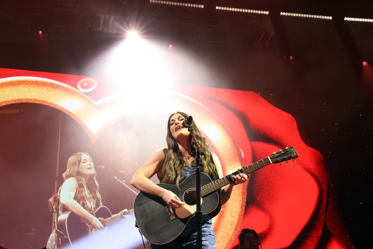 A woman plays acoustic guitar and sings onstage