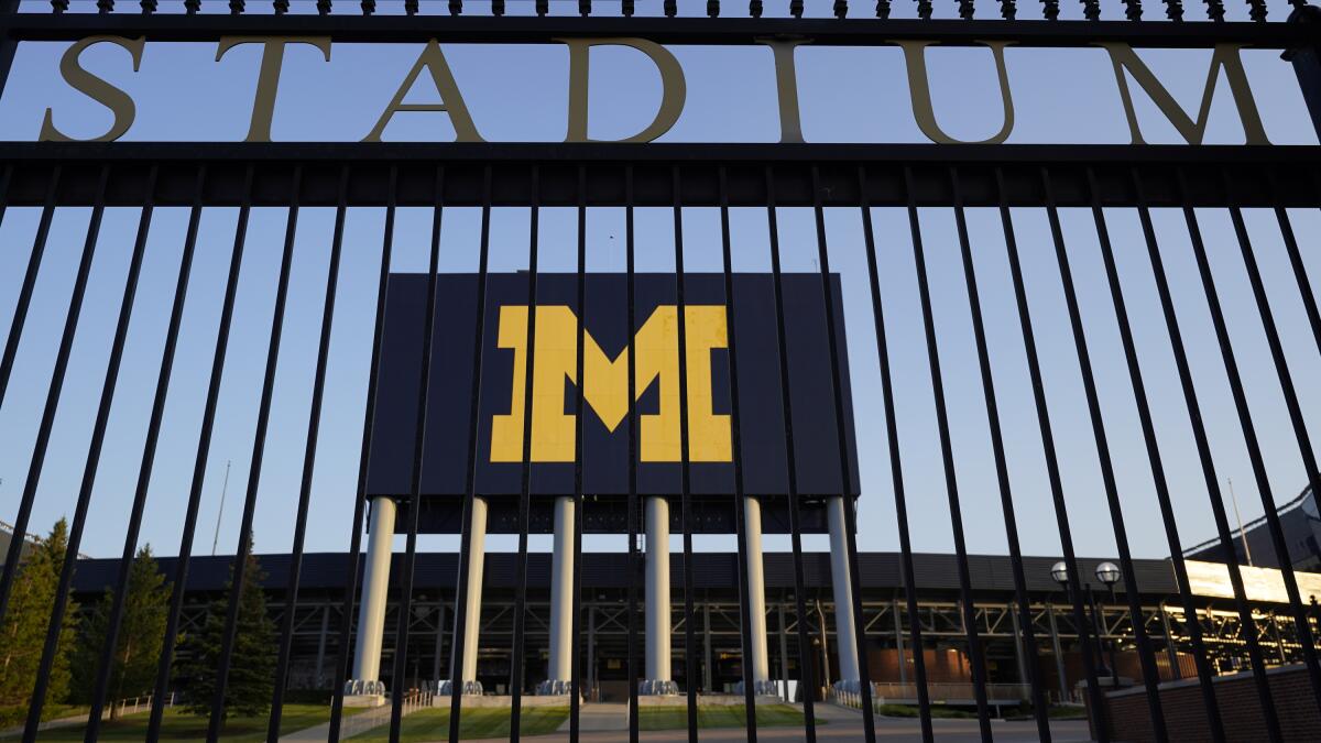 A large, elevated sign of an "M" against a dark blue background is seen behind a fence with the word Stadium 