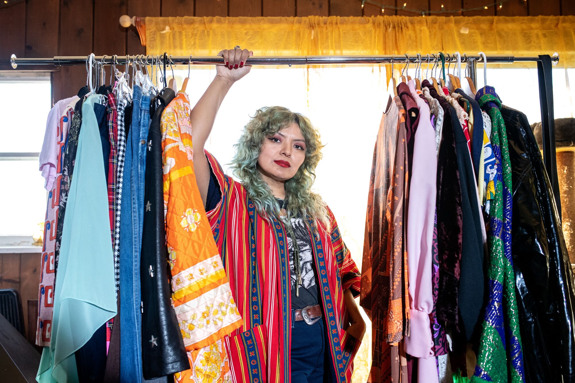 Rebecca Recinos wears a vintage patterned kimono and rests her hand on the bar of a clothing rack