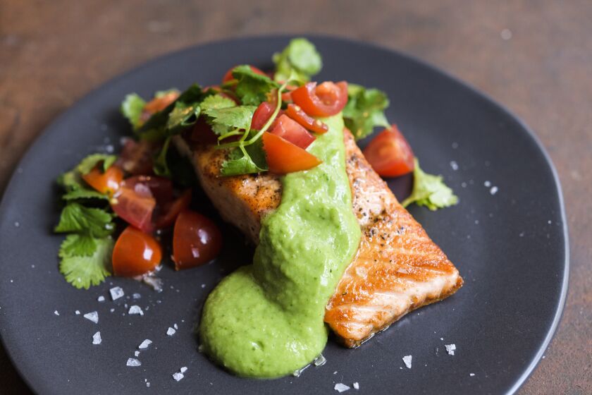 A piece of salmon with a green avocado sauce and tomato salsa.